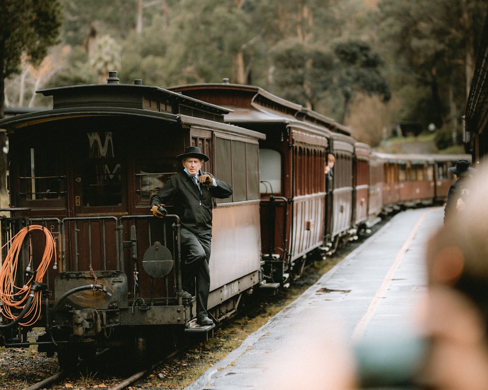 a man in a suit and hat standing on the side of a train