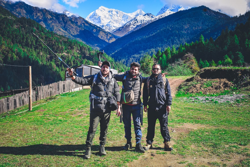 three people standing in a field with mountains in the background