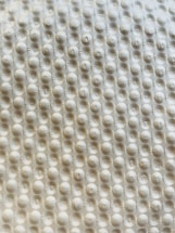 A textured surface with a repetitive pattern of raised circular bumps, resembling a bubble wrap or embossed material. The lighting casts subtle shadows, highlighting the three-dimensional quality of the texture.