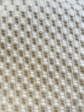 A textured surface with a repetitive pattern of raised circular bumps, resembling a bubble wrap or embossed material. The lighting casts subtle shadows, highlighting the three-dimensional quality of the texture.