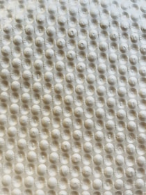 A textured surface with a repetitive pattern of raised circular bumps, resembling a bubble wrap or embossed material. The lighting casts subtle shadows, highlighting the three-dimensional quality of the texture.