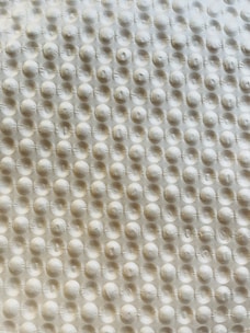 A textured surface with a repetitive pattern of raised circular bumps, resembling a bubble wrap or embossed material. The lighting casts subtle shadows, highlighting the three-dimensional quality of the texture.