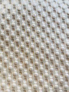 A textured surface with a repetitive pattern of raised circular bumps, resembling a bubble wrap or embossed material. The lighting casts subtle shadows, highlighting the three-dimensional quality of the texture.