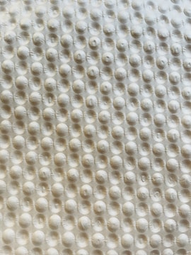 A textured surface with a repetitive pattern of raised circular bumps, resembling a bubble wrap or embossed material. The lighting casts subtle shadows, highlighting the three-dimensional quality of the texture.