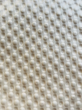 A textured surface with a repetitive pattern of raised circular bumps, resembling a bubble wrap or embossed material. The lighting casts subtle shadows, highlighting the three-dimensional quality of the texture.