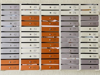 A grid of numbered mailboxes arranged in several columns, each containing multiple slots. Some of the mailboxes have letters and papers sticking out of them. The mailboxes are colored in shades of white, grey, and orange, and each slot is labeled with a different number.