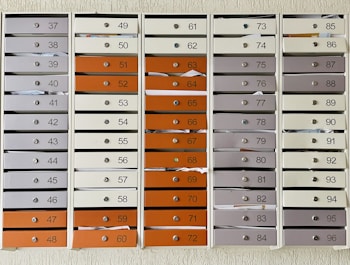 A grid of numbered mailboxes arranged in several columns, each containing multiple slots. Some of the mailboxes have letters and papers sticking out of them. The mailboxes are colored in shades of white, grey, and orange, and each slot is labeled with a different number.