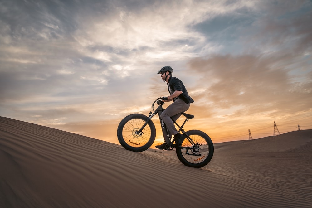 a man riding a bike on top of a sandy hill