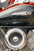 A close-up view of a motorcycle engine, specifically highlighting the Drag Star branding on the black metal surface. The engine features polished chrome components, including a circular emblem with the number 1100 on it.