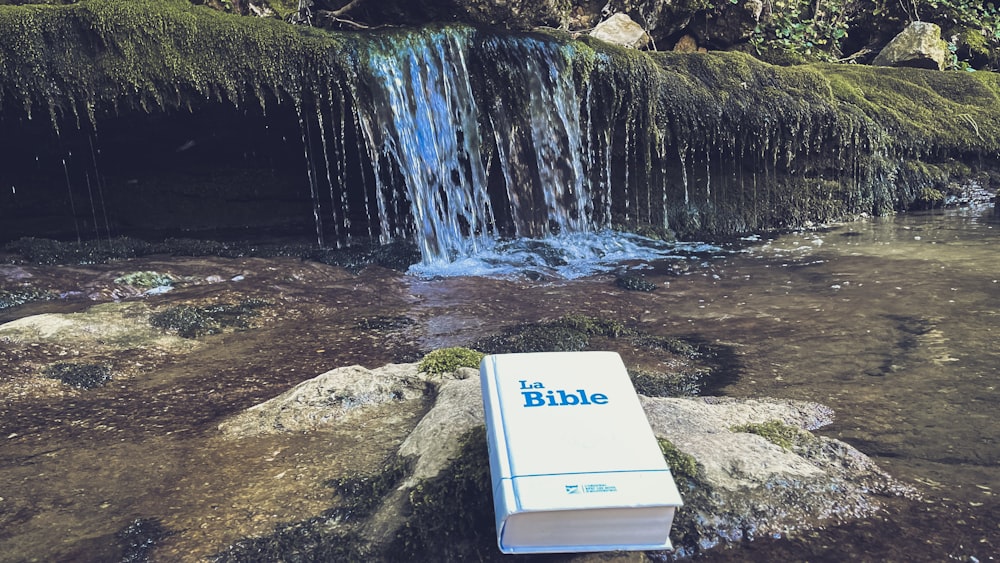 a bible laying on a rock in front of a waterfall