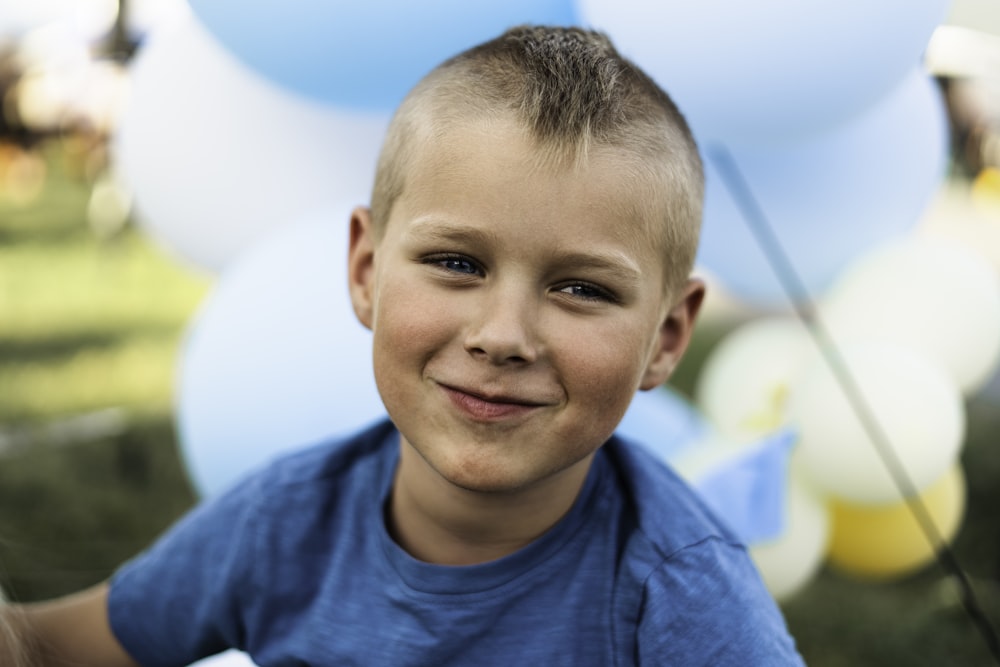 a young boy smiles at the camera with balloons in the background