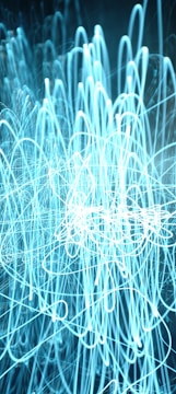 A chaotic mesh of light trails forming intricate loops and overlapping patterns against a dark background. The lines are predominantly blue and white, suggesting motion and a dynamic energy.