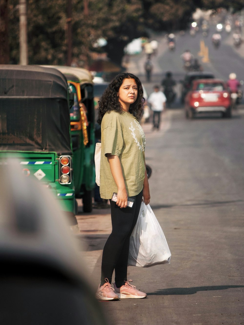 a woman standing on the side of a road holding a bag