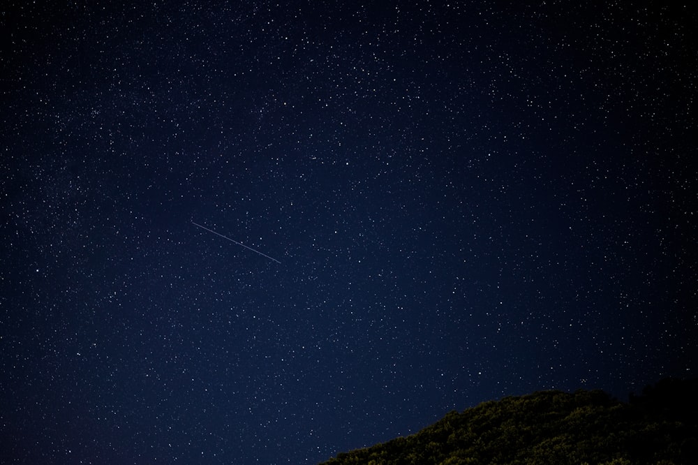 a night sky with stars and a plane in the distance