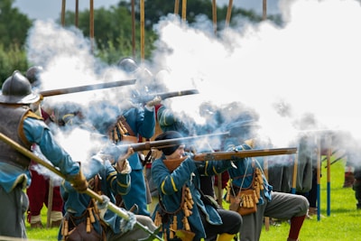 Group of reenactors dressed in period uniforms handling replica muskets in a battlescene.