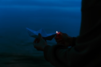 Close-up of hands releasing a small paper boat into flowing river water.