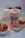 A pink smoothie drink is surrounded by fresh strawberries in a bowl, a bottle of milk, and a small cactus plant. The drink is topped with banana and strawberry slices and is placed on a textured fabric, possibly burlap.