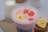 A creamy pink smoothie topped with banana and strawberry slices in a clear plastic cup. In the background, there's a glass bottle of milk and a few banana slices on a wooden board.