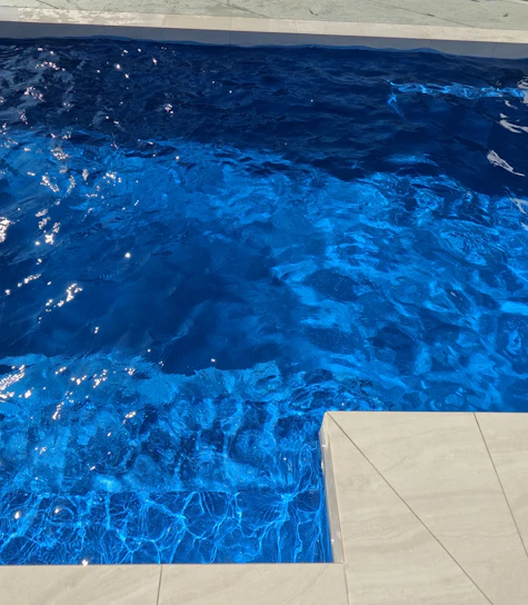 A professional technician cleaning a sparkling swimming pool under bright sunlight.