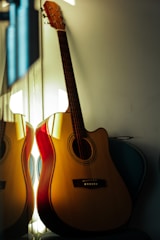 Close-up of a vintage acoustic guitar resting against a wooden wall, warm sunlight highlighting its curves.