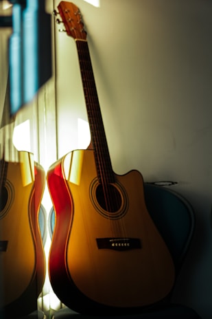 An acoustic guitar leaning gently against a dark blue-gray wall, bathed in warm ambient light.