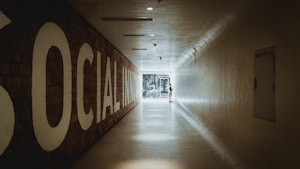 A long, tiled hallway with a large sign on the left reading 'SOCIAL INNOVATION,' leading towards a bright, glass doorway at the end. A person is standing near the doorway, interacting with something on the wall.