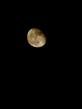 A luminous, partially illuminated moon set against a completely dark background. The lunar surface shows distinct craters and shading, indicating the moon's textured appearance.