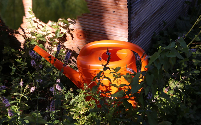 A vibrant watering can resting beside blooming flowers in a sunlit garden.