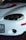 Close-up of the front of a white car with a prominent headlight, a bumper with an orange indicator light, a license plate reading 'GP', and a decal with a stylized design in red and black.