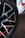 A close-up view of a car wheel with a stylish alloy rim. The wheel features a sleek black and silver spoke design with red accents visible through the spaces in the rim. The tire is branded with 'Hankook,' a well-known tire manufacturer.