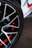 A close-up view of a car wheel with a stylish alloy rim. The wheel features a sleek black and silver spoke design with red accents visible through the spaces in the rim. The tire is branded with 'Hankook,' a well-known tire manufacturer.