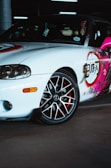 A sporty car with decorative graphics on the side panel, featuring a mix of bold colors and intricate patterns. The car's wheel has a glossy finish with a contrast of black and red elements.