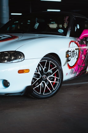 A sporty car with decorative graphics on the side panel, featuring a mix of bold colors and intricate patterns. The car's wheel has a glossy finish with a contrast of black and red elements.