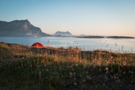 A vibrant camping tent pitched beside a serene mountain stream under clear blue skies.