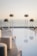 A beautifully arranged outdoor setting with a reflective pool surrounded by tall glass candle holders. Elegant white seating and elevated floral arrangements stand against a serene ocean backdrop under a clear sky.