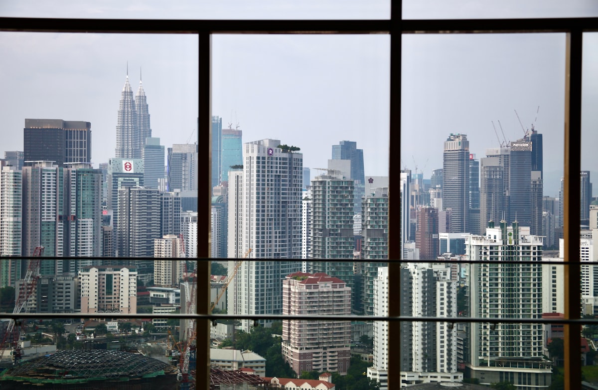 The Kuala Lumpur skyline through a large dark-framed window, residential towers and the Petronas Twin Towers in the distance