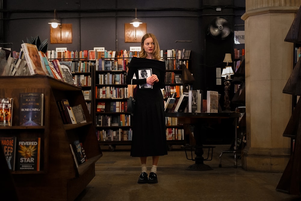 a woman standing in a library holding a book