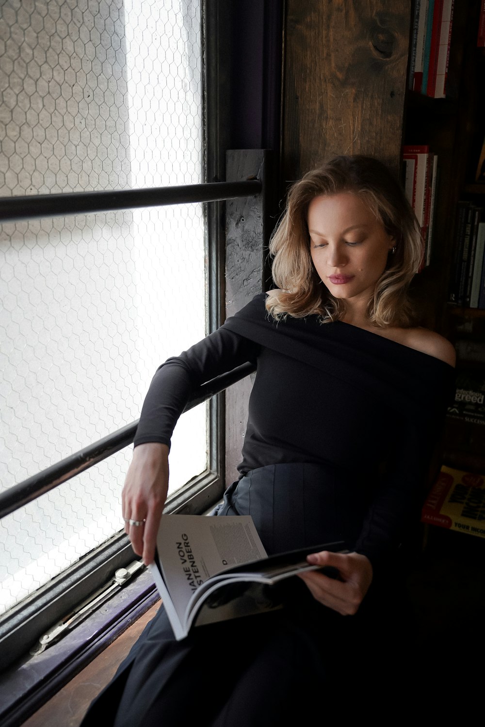 a woman sitting on a window sill reading a book