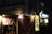 A dimly lit street scene featuring traditional Japanese architecture with illuminated signs and banners. The storefronts display a variety of colorful food images, suggesting a focus on seafood cuisine. There are paper lanterns and wooden accents, creating a cozy and inviting atmosphere.