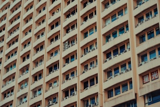 A tall building with multiple rows of windows, each equipped with air conditioning units. The facade is a beige color, and there are signs with Asian script on them, adding cultural context to the scene.