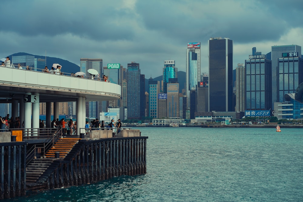 a group of people standing on top of a pier next to a body of water