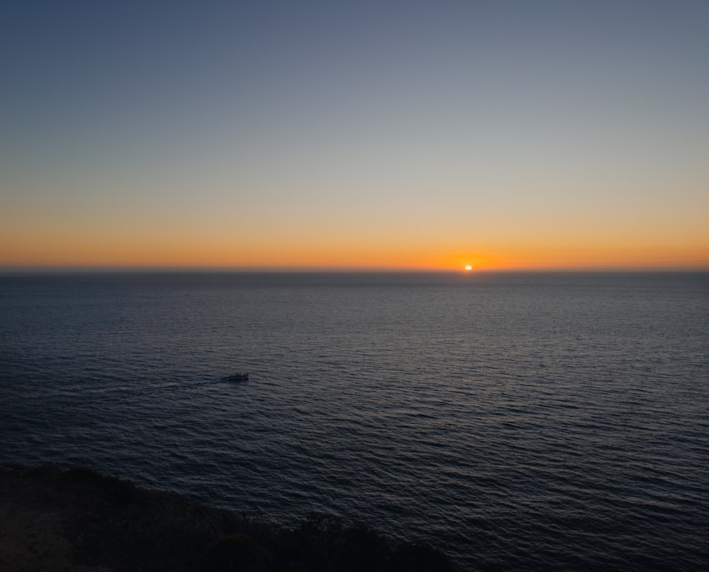 the sun is setting over the ocean with a boat in the water