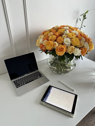 A warm and inviting workspace with a vase of fresh flowers next to a laptop and notebook.
