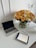 A clean and modern workspace featuring a closed laptop, an electronic tablet displaying handwritten notes, and a stylus pen on a white table. A large, vibrant bouquet of yellow, orange, and white roses in a glass vase adds a colorful and fresh element to the setting.