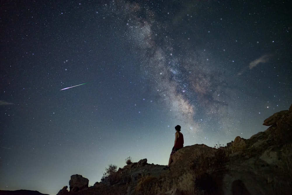 a person sitting on a rock looking up at the stars