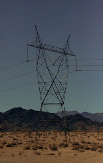 High-voltage transmission towers stretching across a desert landscape under a clear blue sky.