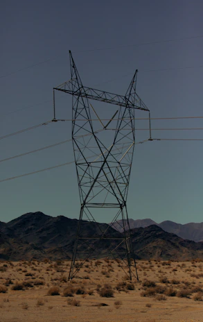 High-voltage transmission towers stretching across a desert landscape under a clear blue sky.