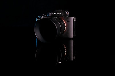 A high-end digital camera with a lens, featuring the Sony logo on a dark, reflective surface. The camera body is primarily black with a subtle sheen, highlighting its sleek design and modern technology.
