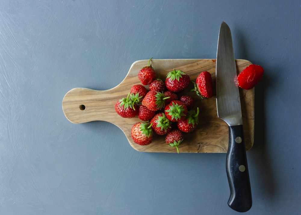 a cutting board with a knife and a bunch of strawberries