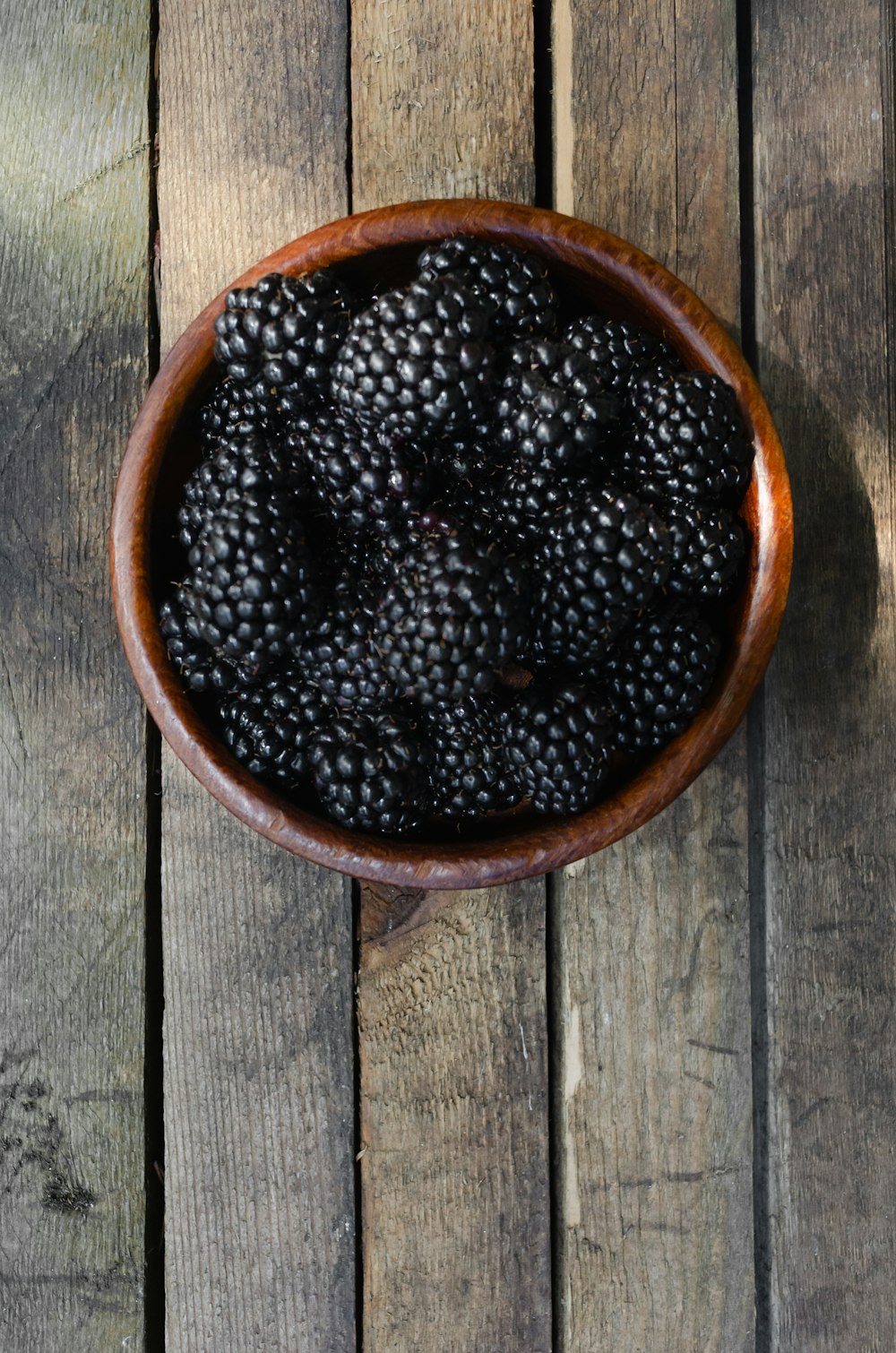 a wooden bowl filled with blackberries on top of a wooden table